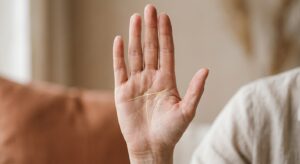 A close-up, highly detailed photograph of an open human palm held upright against a soft, warm-toned neutral background. The palm displays clearly visible hand lines, with two prominent lines — a head line and a heart line — connected by a subtle bridging line, illustrating a modified simian crease formation. The lines are rendered with fine, realistic skin texture and natural lighting that emphasizes the depth and clarity of the creases. Overlaid on the palm are faint, elegant glowing golden tracings highlighting the specific line patterns and their connections, giving a professional, analytical feel. The mood is calm, thoughtful, and authoritative — evoking the expertise of a seasoned palmistry practitioner. The overall aesthetic is clean and editorial, with soft bokeh in the background, suitable for a professional palmistry education article.
