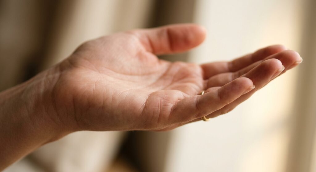 A close-up editorial photograph of an open human palm held gently under warm, soft natural light, with the focus on the small delicate lines near the base of the pinky finger. The hand belongs to a woman, skin appearing smooth and naturally lit with golden hour warmth. The lines on the palm are subtly visible — particularly the fine, short horizontal lines on the side of the hand beneath the little finger. The background is softly blurred with warm cream and ivory tones, evoking a calm, introspective, and thoughtful atmosphere. The composition feels intimate and meditative, like a moment of self-discovery. Photorealistic style, shallow depth of field, warm tones, editorial quality.